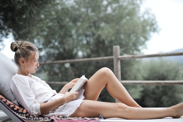 woman lying on white chair while reading book